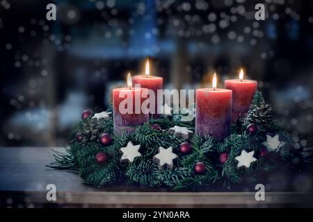 Adventskranz mit vier beleuchteten Kerzen und Weihnachtsdekoration im Freien in einer Terrasse bei Nacht in bläulichem Licht, schneebedecktem Bokeh, Kopierraum, farbiges Foto, s Stockfoto