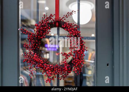 Ein Weihnachtskranz aus roten Beeren ist an einer Ladentür angebracht, was einen festlichen und einladenden Touch verleiht. Stockfoto