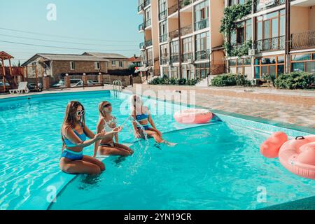 Drei Frauen sitzen in einem Pool mit rosafarbenen und blauen Schwimmbahnen. Die Szene ist unbeschwert und lustig. Stockfoto