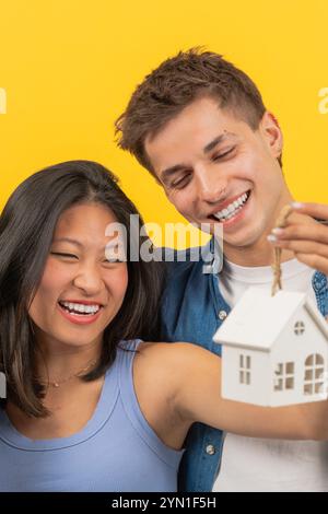 Glückliches Paar, das Hausmodell auf hellgelbem Hintergrund hält. Vertikal Stockfoto