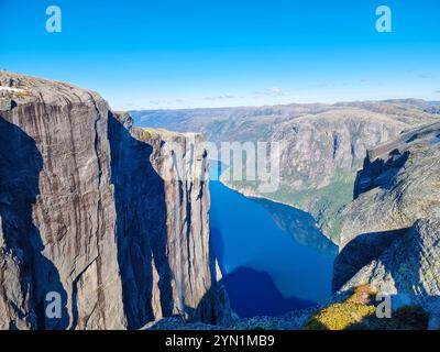 Hoch aufragende Klippen erheben sich dramatisch neben einem ruhigen Fjord und spiegeln den leuchtend blauen Himmel darüber wider. Diese atemberaubende Landschaft wurde bei Tageslicht aufgenommen, kJ Stockfoto