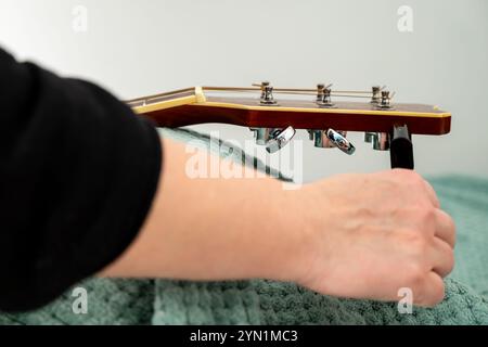 Menschliche Hand, die neue Saiten auf Akustikgitarrenmaschinenköpfen oder Stimmspitzen mit Hilfe von Streicherwickler oder -Wechsler aufwickelt Stockfoto