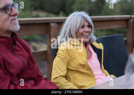 Freimütiges Porträt einer freudigen Frau mittleren Alters mit silbernem Haar, die eine hellgelbe Jacke trägt, während eines geselligen Treffens im Freien. Natürlicher, authentischer Moment Stockfoto