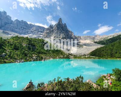 Eingebettet zwischen hohen Gipfeln spiegelt dieser atemberaubende türkisfarbene See den lebendigen Himmel wider, während Besucher die ruhige Landschaft genießen. Üppiges Grün umrahmt das Wasser, Lago Di Sorapis Dolomites Italien Stockfoto