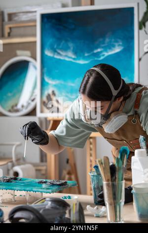 Aufmerksame, gründliche Frau, die sorgfältig mit Epoxidharz arbeitet, um Kunstwerke zu malen. Stockfoto