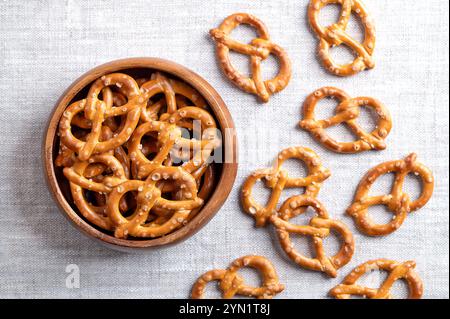 Gesalzene Brezeln in einer Holzschale auf Leinenstoff. Goldene geröstete kleine Brezeln traditioneller Form mit verflochtenen Enden zu einem Brezelbogen. Stockfoto