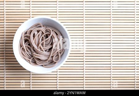 Gekühlte, gekochte Soba-Nudeln in einer weißen Schüssel, auf eine Bambusmatte gelegt. Dünne japanische Nudeln, hauptsächlich aus Buchweizenmehl hergestellt. Stockfoto