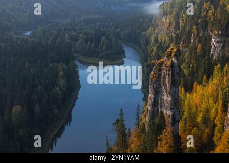 Der sich windende Fluss fließt anmutig durch einen üppigen Wald, der mit lebhaften Herbstfarben geschmückt ist und in das sanfte Licht der Dämmerung getaucht ist, was eine friedliche nat schafft Stockfoto