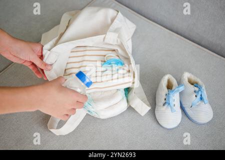 Eine Tasche für Mutter mit Neugeborenen auf einem grauen Sofa. Eine Frau steckt Kindersachen in ihre Handtasche Stockfoto