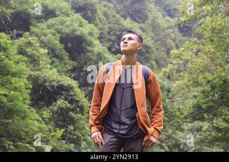 Porträt eines jungen, asiatischen Backpackers, der mitten im Wald reist. Selbstbewusster Mann, der sich umsieht, während er in der Natur mit aufgeregten Expressen spaziert Stockfoto