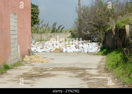 Bauschutt und Müll verschmutzen eine Straße in der Nähe eines verlassenen Gebäudes, wobei Umweltschäden und illegale Deponien hervorgehoben werden Stockfoto