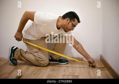 Erwachsener Mann mit einem Maßband, der einen Parkett-Laminatboden in einem Unternehmen installiert Stockfoto