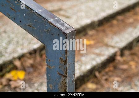 Verwittertes Metallgeländer mit Rost, Verfall und abblätternder Farbe mit verschwommenen Steinstufen im Hintergrund Stockfoto