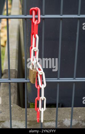 Rot-weiße Kunststoffkette und Vorhängeschloss aus Metall zur Sicherung eines Metallzauns Stockfoto