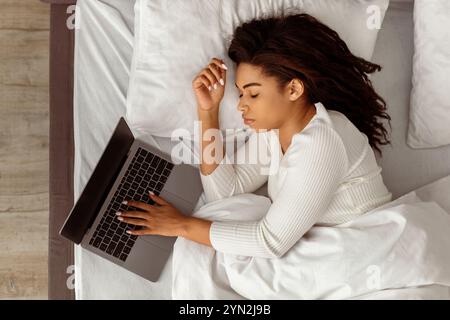 Afroamerikanische Frau liegt im Bett, schläft und hält einen Laptop Stockfoto
