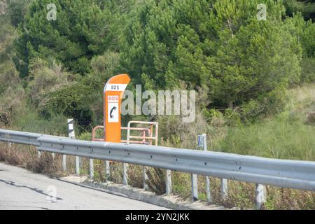 Oranges Notruftelefon mit sos-Signal und Nummer 825 auf einer Autobahn mit Leitplanke und Wald im Hintergrund Stockfoto