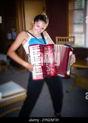 Ein Mädchen, das so tut, als würde er im Wohnzimmer der Großeltern Akkordeon spielen, während er in Ludington, Michigan, USA, reist. Stockfoto