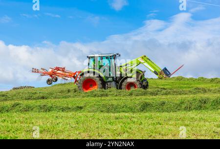 Der Landwirt fährt seinen Traktor mit einer Ballengabel und dreht das geschnittene Heu, damit es im Sommer trocken und bereit für die Ballenherstellung ist. Yorkshire Dales, Großbritannien. Horizontaler Whirlpool Stockfoto