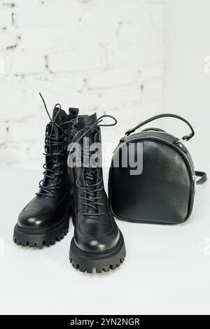 Schwarze Lederstiefel für Damen und ein schwarzer Lederrucksack stehen auf weißem Hintergrund. Damenmode Stockfoto