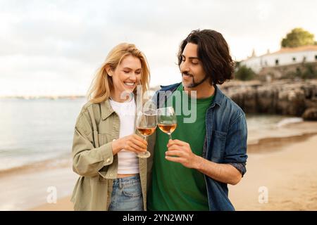 Paare genießen den Sonnenuntergang am Strand, während sie mit einem Glas Wein rösten Stockfoto