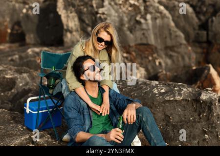 Ein Paar genießt einen entspannenden Tag an der felsigen Küste mit einem Getränk in der Hand Stockfoto