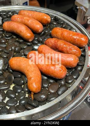 Gegrillte Schweinefleischwurst mit dickem Geschmack, die auf schwarzen heißen Steinchen gekocht wird, um sie warm zu halten. Scarlett-Supermarkt. Chinesische Marke. Singapur. Stockfoto