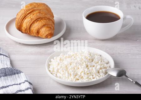 Köstliches Frühstück mit Croissant, Hüttenkäse und Kaffee auf einem Holztisch Stockfoto