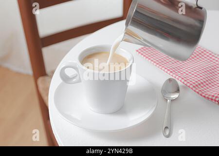 Kaffee mit Milch in einer weißen Tasse auf einer Untertasse auf einem weißen Holztisch. Stockfoto