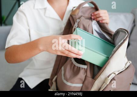 Ein Mädchen steckt eine Lunchbox in einen Schulrucksack. Stockfoto