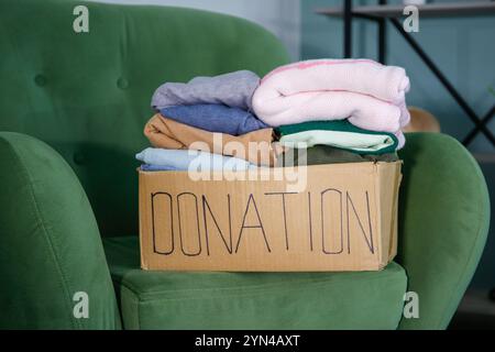 Spendenbox mit Kleidung auf dem Sessel im Wohnzimmer. Stockfoto