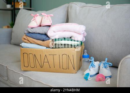 Spendenbox mit Kleidung für Neugeborene auf der Couch im Wohnzimmer. Stockfoto