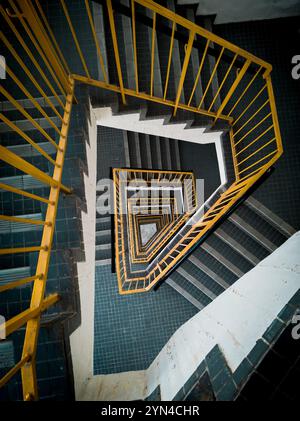 „Abstrakte Perspektive der Wendeltreppe mit gelben Schienen und geometrischen Fliesenmustern im Urban Interior Design“ Stockfoto