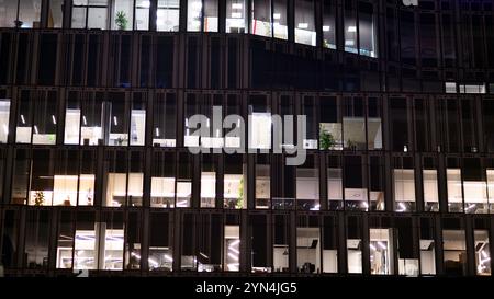 Bürogebäude am Abend mit beleuchteten Arbeitsplätzen. Moderner, verglaster Wolkenkratzer im Finanzviertel. Späte Öffnungszeiten im Büro. Stockfoto