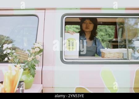 Asiatischer Mitarbeiter von Food Truck, der Papierkarte mit QR-Code im Lieferwagen einstellt Stockfoto