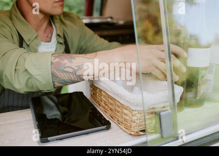 Mittlere Nahaufnahme von tätowierten Händen, die Sirupe für Kaffee und Tee auf dem Tisch im Food Truck einstellen Stockfoto