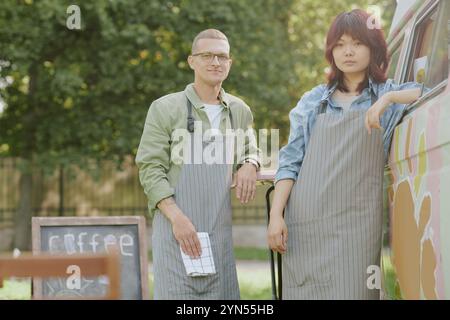 Porträt von kaukasischen und asiatischen Kollegen, die sich auf Tisch und Food Truck stützen, während sie gemeinsam unter freiem Himmel für ein Foto posieren Stockfoto