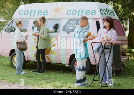 Vier Menschen, die leckeres Fast Food genießen, das im Food Truck hinter ihnen gekauft wurde Stockfoto