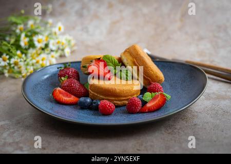 Flauschige Gourmet-Pfannkuchen, serviert auf einem stilvollen blauen Teller mit frischen Beeren und Minzblättern. Elegantes Frühstück, Sommerdessert und Naturkost Stockfoto