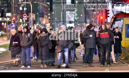 Warschau, Polen. 21. November 2024. Straßenfotografie von Menschen auf der Straße in der Nacht. Die Fußgänger-Silhouetten auf dem Hintergrund des modernen Gebäudes. Stockfoto