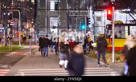 Warschau, Polen. 21. November 2024. Straßenfotografie von Menschen auf der Straße in der Nacht. Die Fußgänger-Silhouetten auf dem Hintergrund des modernen Gebäudes. Stockfoto