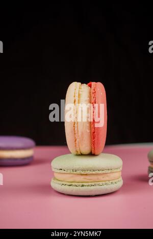 Eine bunte Auswahl an Macarons auf einer Basis mit einem weichen rosa Hintergrund. Dieses delikate französische Gebäck zeigt Eleganz und Geschmack, perfekt für Stockfoto