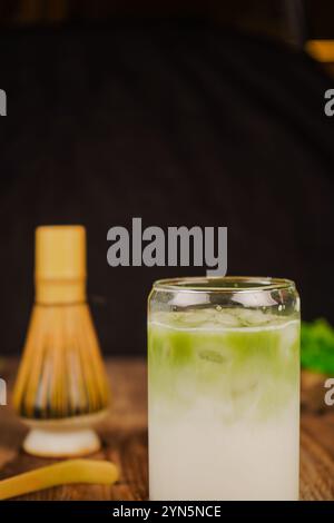 Eine Nahaufnahme eines Bambus-Matcha-Schneebesen auf einem Matcha-Tisch, der Achtsamkeit und Tradition symbolisiert. Ein volles Glas gefrorener Matcha Latte Stockfoto