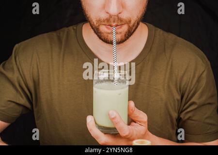 Nahaufnahme eines Mannes, der grünen Matcha Latte aus einem Glas durch ein Strohhalm trinkt, Teekulturkonzept. Ein Mann schlürft Tee durch einen Strohhalm Stockfoto