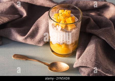 Chia Samenpudding, Mangopüree und Kokosmilch auf dem Tisch mit Löffel und grauer Serviette. Gesundes Frühstückskonzept, vegane, zuckerfreie Rohdesserts Stockfoto