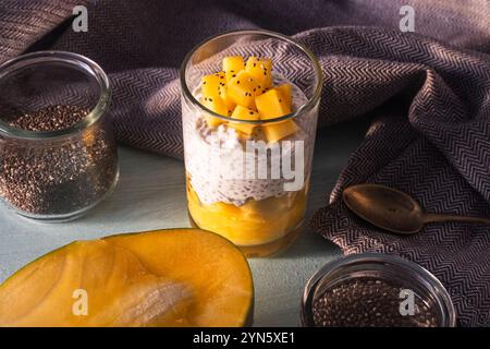 Chia Samenpudding, Mangopüree und Kokosmilch auf dem Tisch mit Löffel und grauer Serviette. Gesundes Frühstückskonzept, vegane, zuckerfreie Rohdesserts Stockfoto