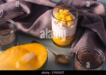 Chia Samenpudding, Mangopüree und Kokosmilch auf dem Tisch mit Löffel und grauer Serviette. Gesundes Frühstückskonzept, vegane, zuckerfreie Rohdesserts Stockfoto