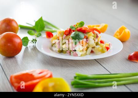 Gemüsesalat aus gekochtem Gemüse, mit Erbsen, Wurst, süßem Pfeffer. Auf einem Holztisch. Stockfoto