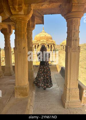 Frau von hinten, die auf gelbe Sandsteincenotaphs in Bada Bagh in Jaisalmer, Indien, blickt Stockfoto