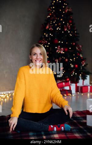 Schöne blonde Frau lächelt an dem Weihnachtsbaum mit Geschenken für Neujahr Stockfoto