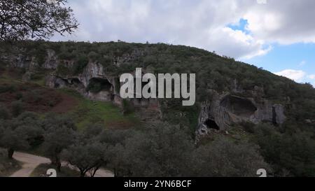 Buracas do Casmilo in Condeixa - Portugal. Alte Kalksteinhöhlen in einem zerklüfteten Hügel mit mehreren natürlichen Höhlenöffnungen im Grün Stockfoto